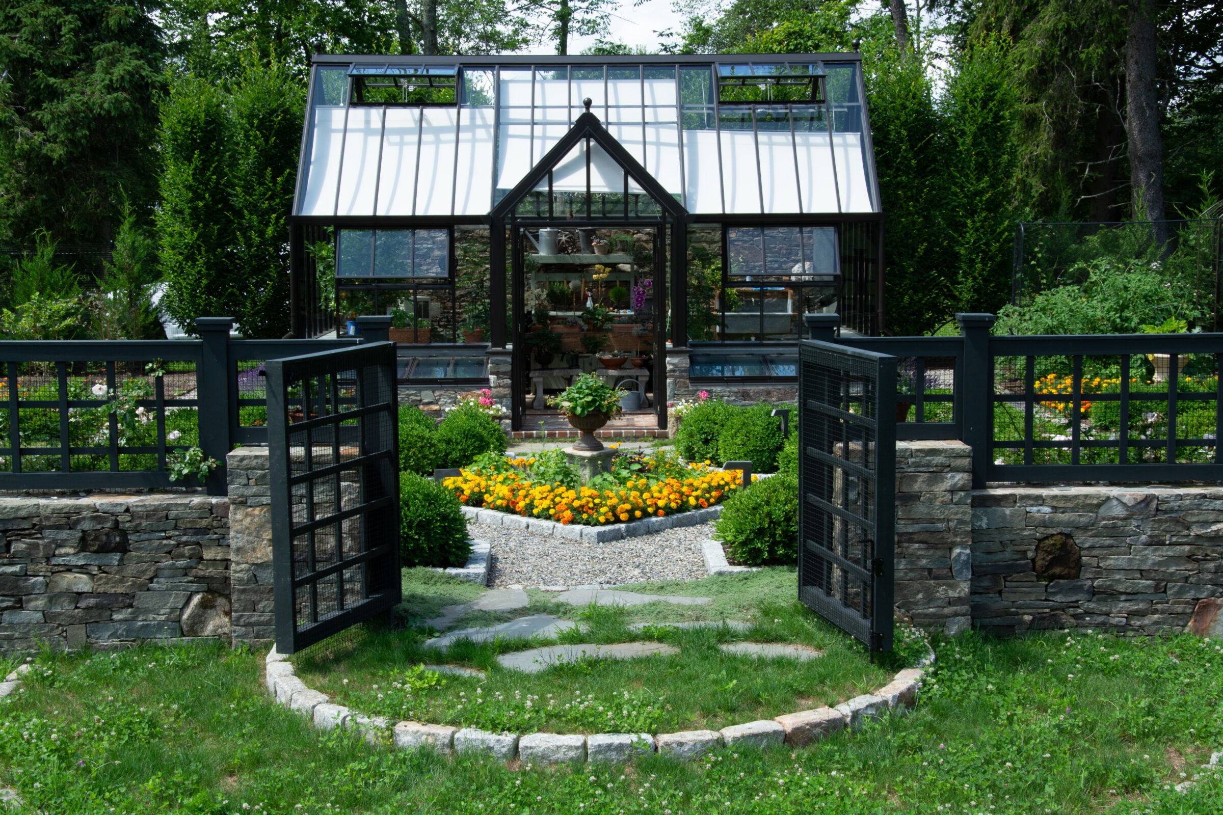 An inviting garden scene with an open gate leading to a path that ends at a charming glass greenhouse surrounded by lush vegetation and flowers.
